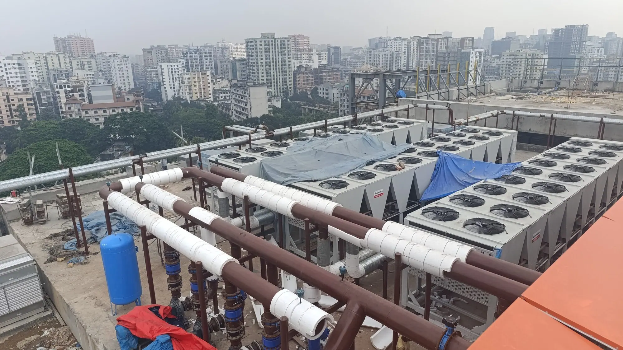 Rooftop air-cooled chiller plant with insulated chilled-water pipework on a Dhaka building